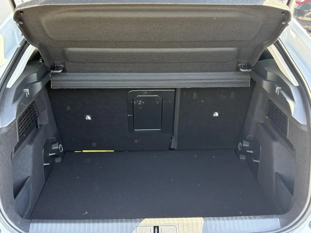 Coffre ouvert vu de l'arrière d'une Citroën C4 blanche, montrant un espace de chargement noir et une trappe centrale.