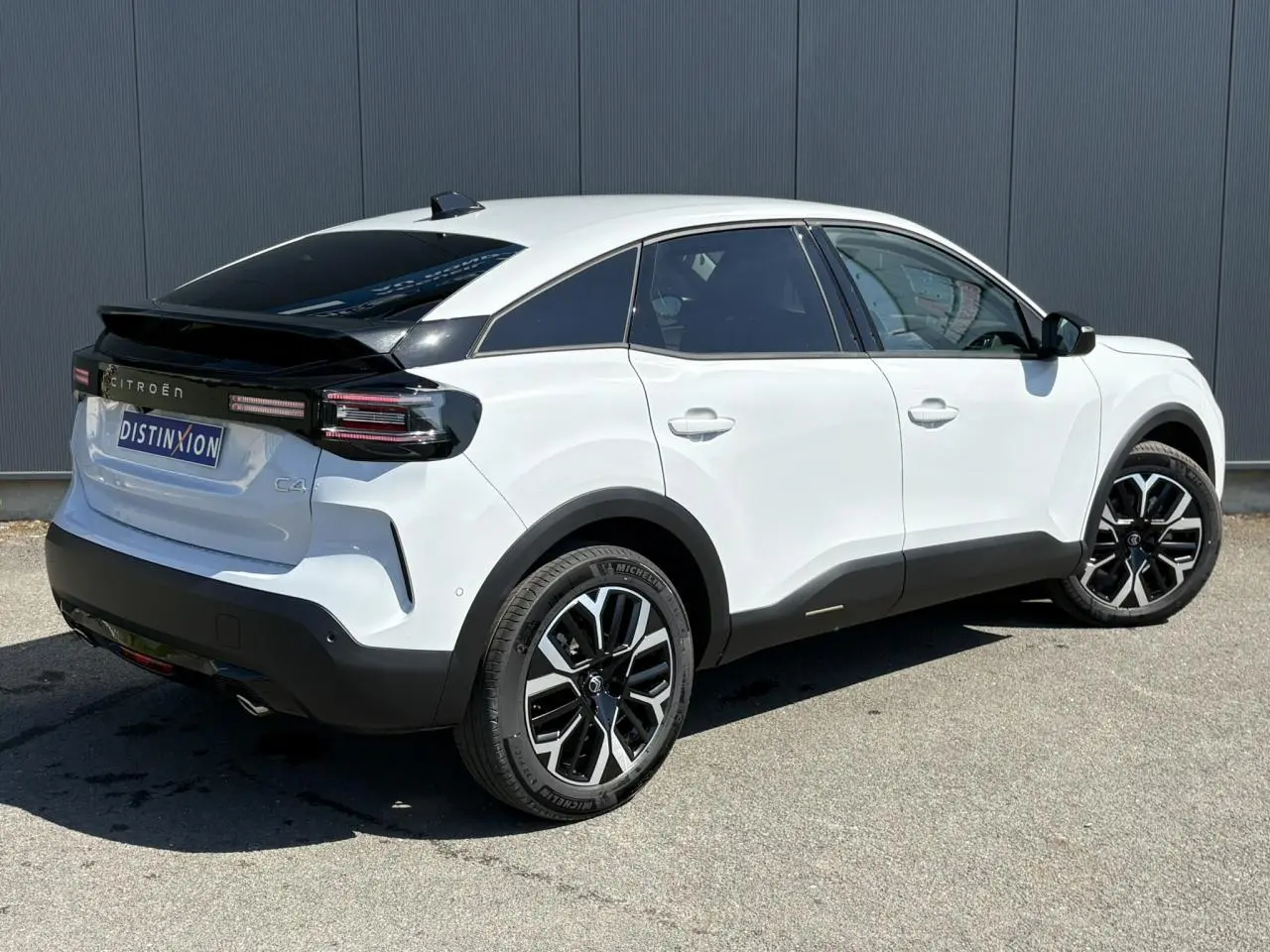 Vue 3/4 arrière droite d'une Citroën C4 Hybrid 145 blanche Okénite avec jantes alliage 18'' et toit noir contrasté.