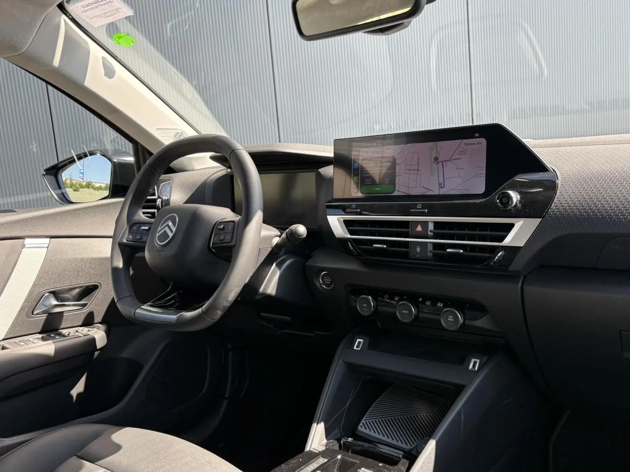 Vue intérieure côté conducteur de la Citroën C4 Hybrid 2025, avec tableau de bord noir et écran tactile GPS allumé.