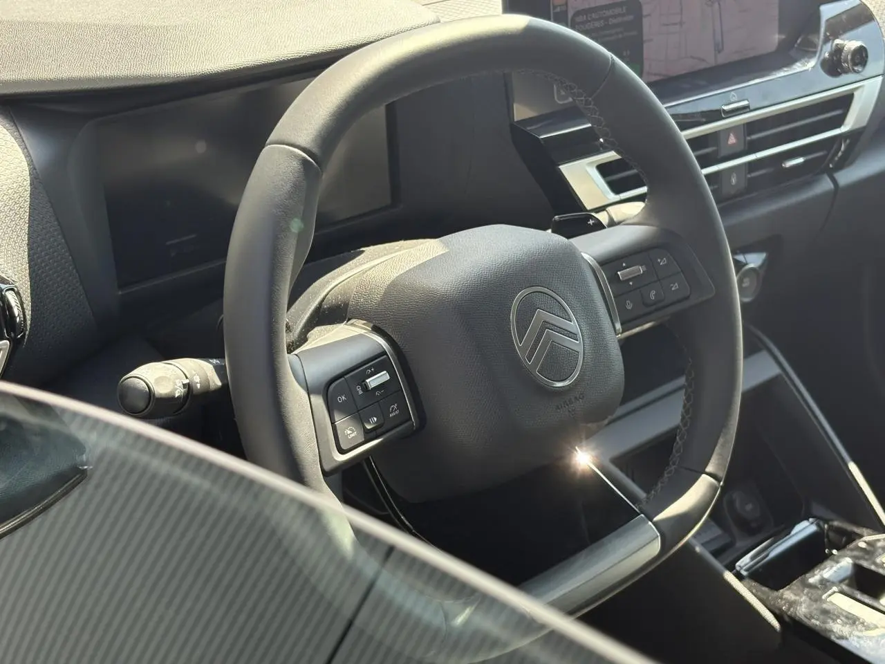 Vue rapprochée du volant cuir noir avec commandes intégrées du tableau de bord intérieur de la Citroën C4 Hybrid 2025.
