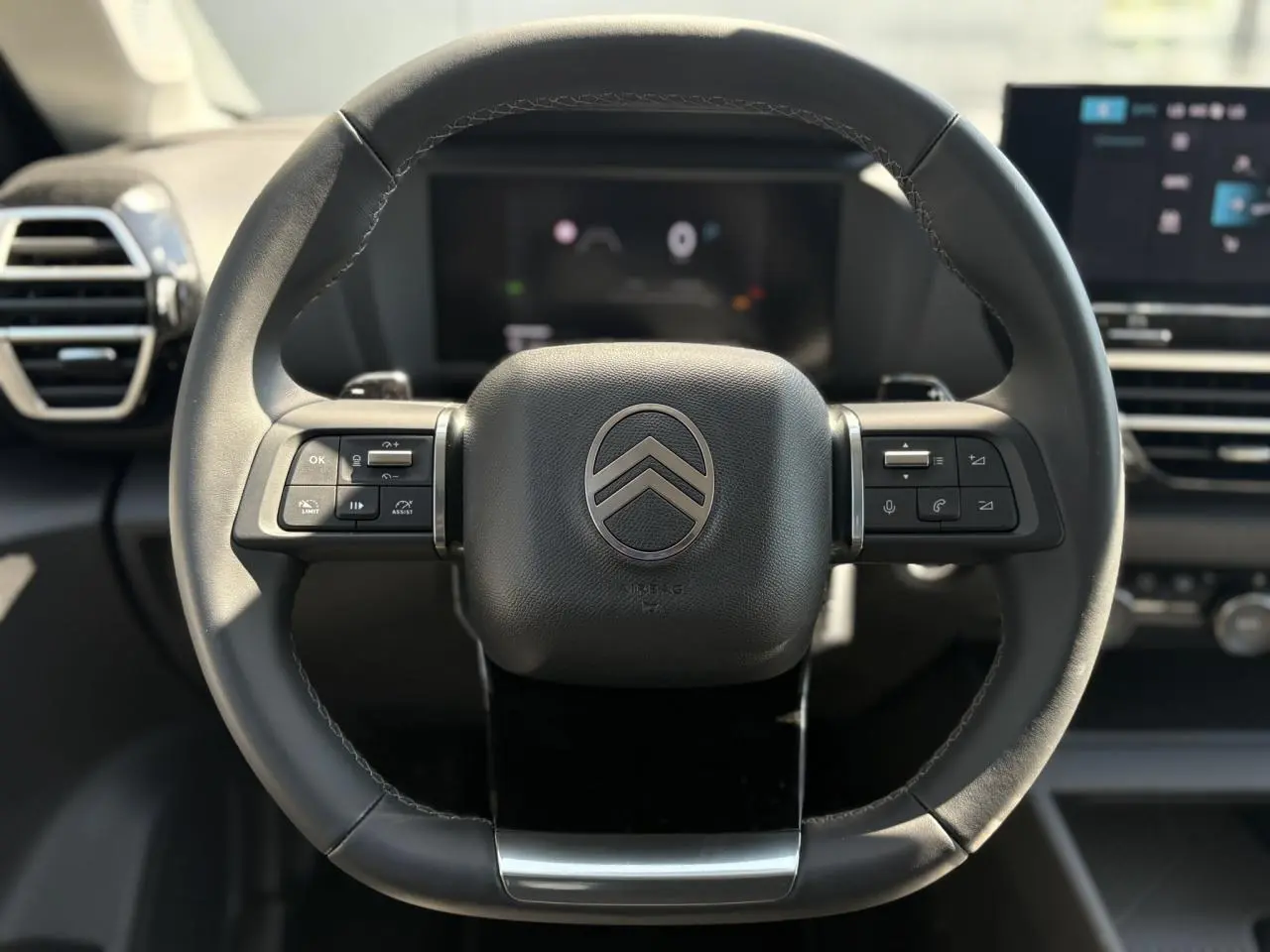 Volant cuir noir Citroën C4 Hybrid 145 vu de face avec commandes intégrées et tableau de bord numérique flou en arrière-plan.
