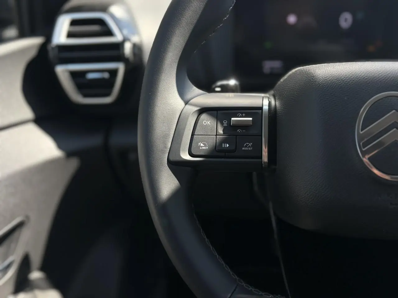 Gros plan sur le volant cuir noir côté gauche du Citroën C4 Hybrid 2025 avec commandes intégrées et logo central.