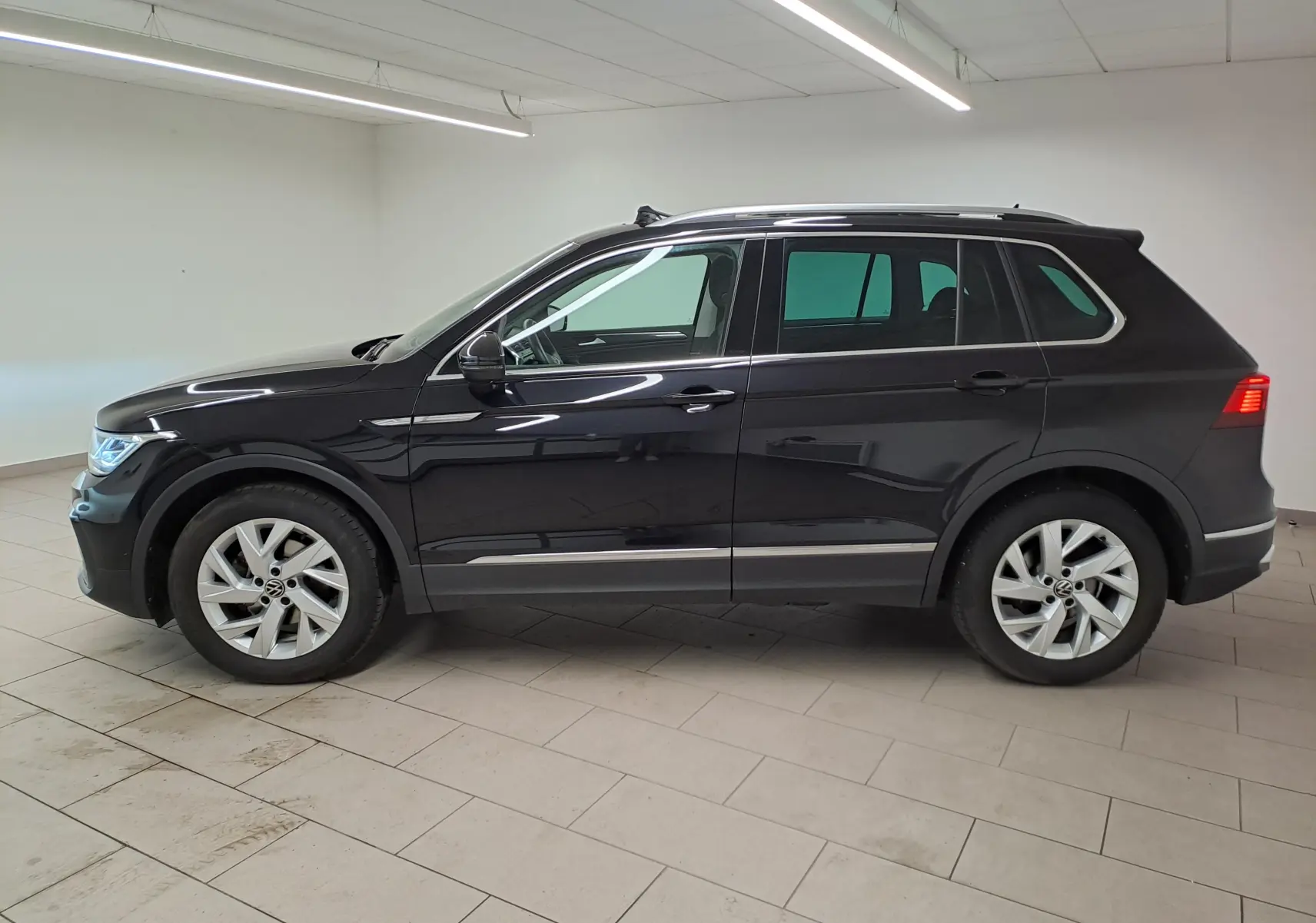 Volkswagen Tiguan noir intense vu de profil gauche en intérieur, avec crochet d'attelage escamotable visible à l'arrière.