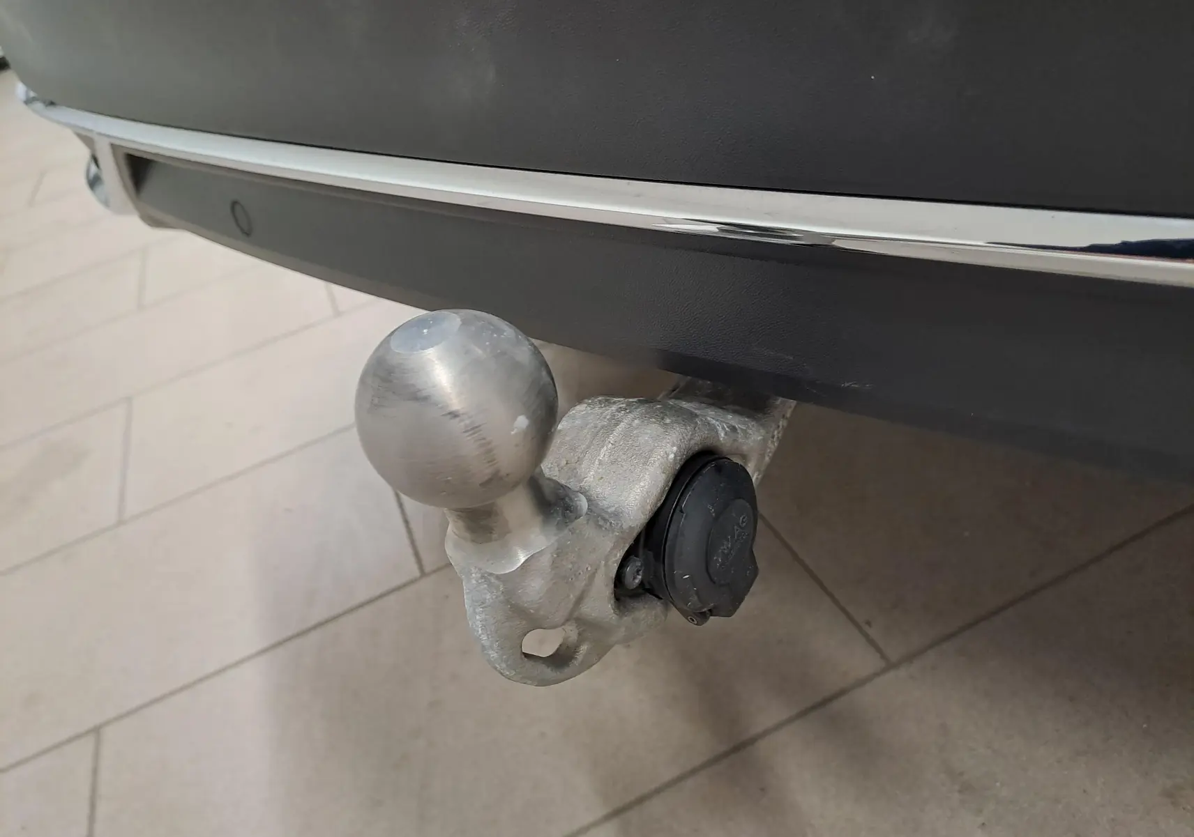 Gros plan sur le crochet d'attelage escamotable en métal fixé sous le pare-chocs arrière noir intense du Volkswagen Tiguan.
