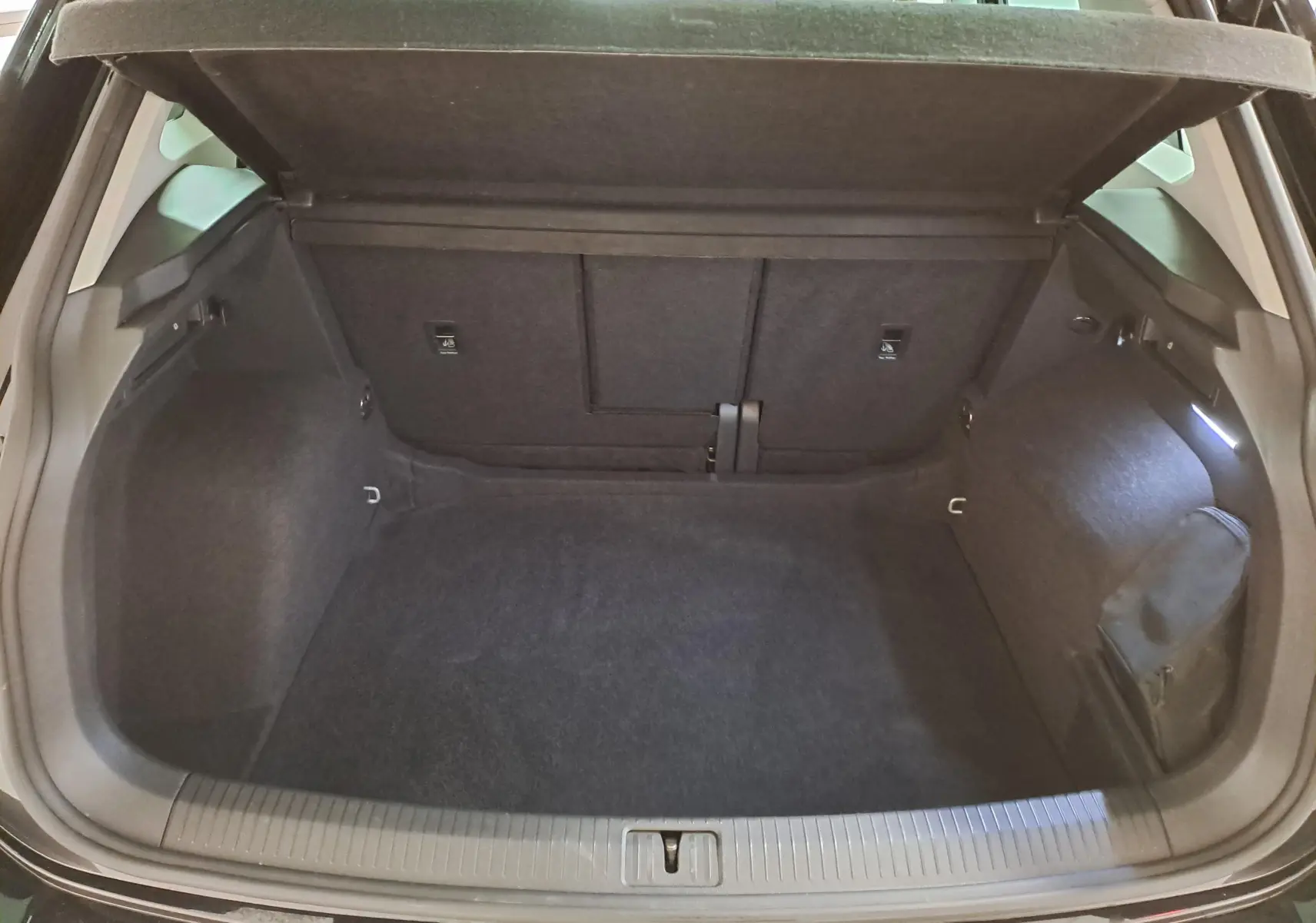 Vue intérieure du coffre ouvert d'un Volkswagen Tiguan noir intense 2022, montrant un espace de rangement propre et spacieux.