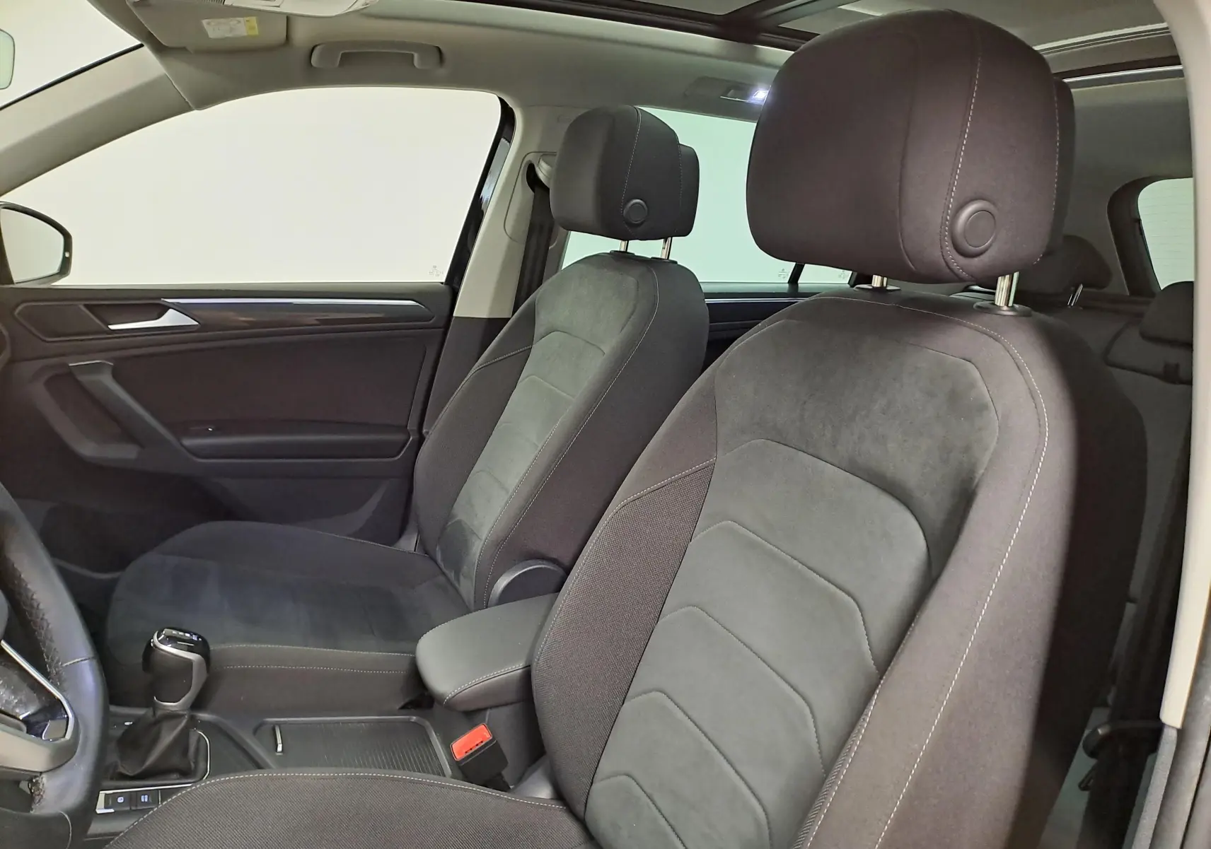 Vue intérieure côté gauche du Volkswagen Tiguan 2022, sièges tissu noir avec surpiqûres blanches et accoudoir central.