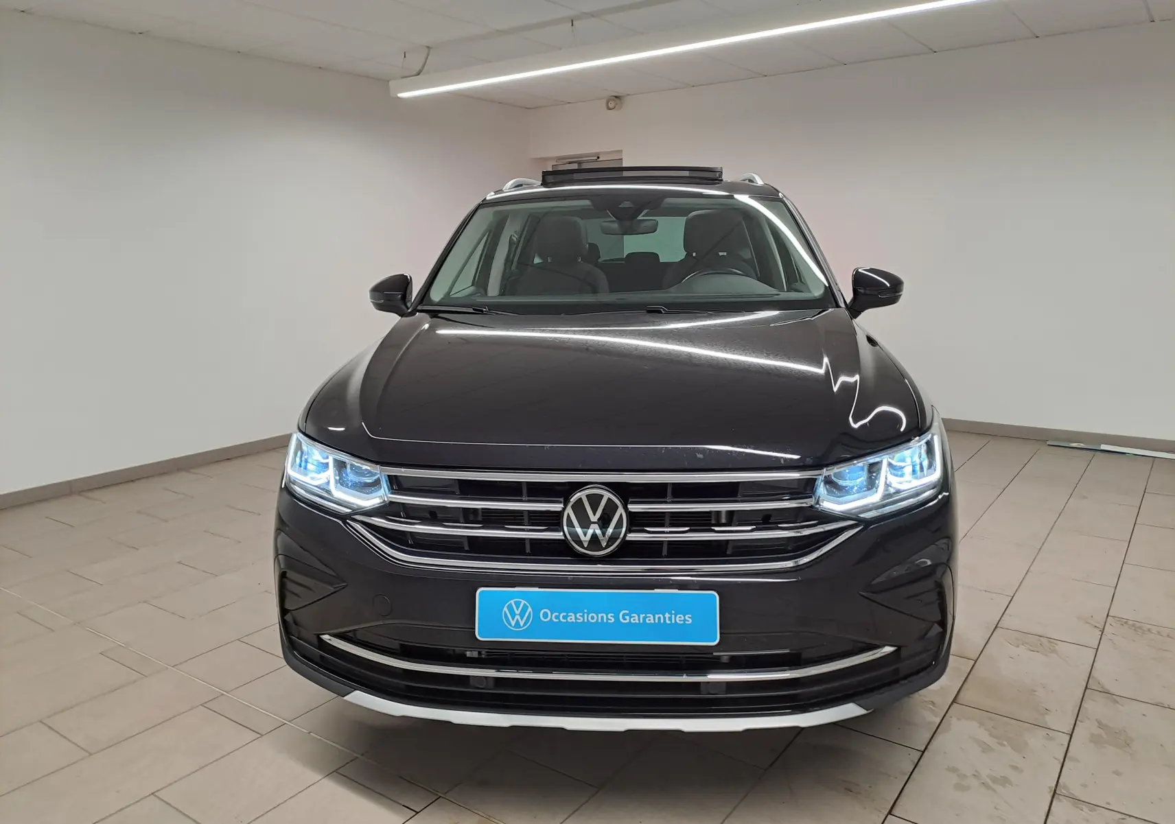 Vue frontale d'un Volkswagen Tiguan noir intense 2022 avec phares allumés et plaque "Occasions Garantis".