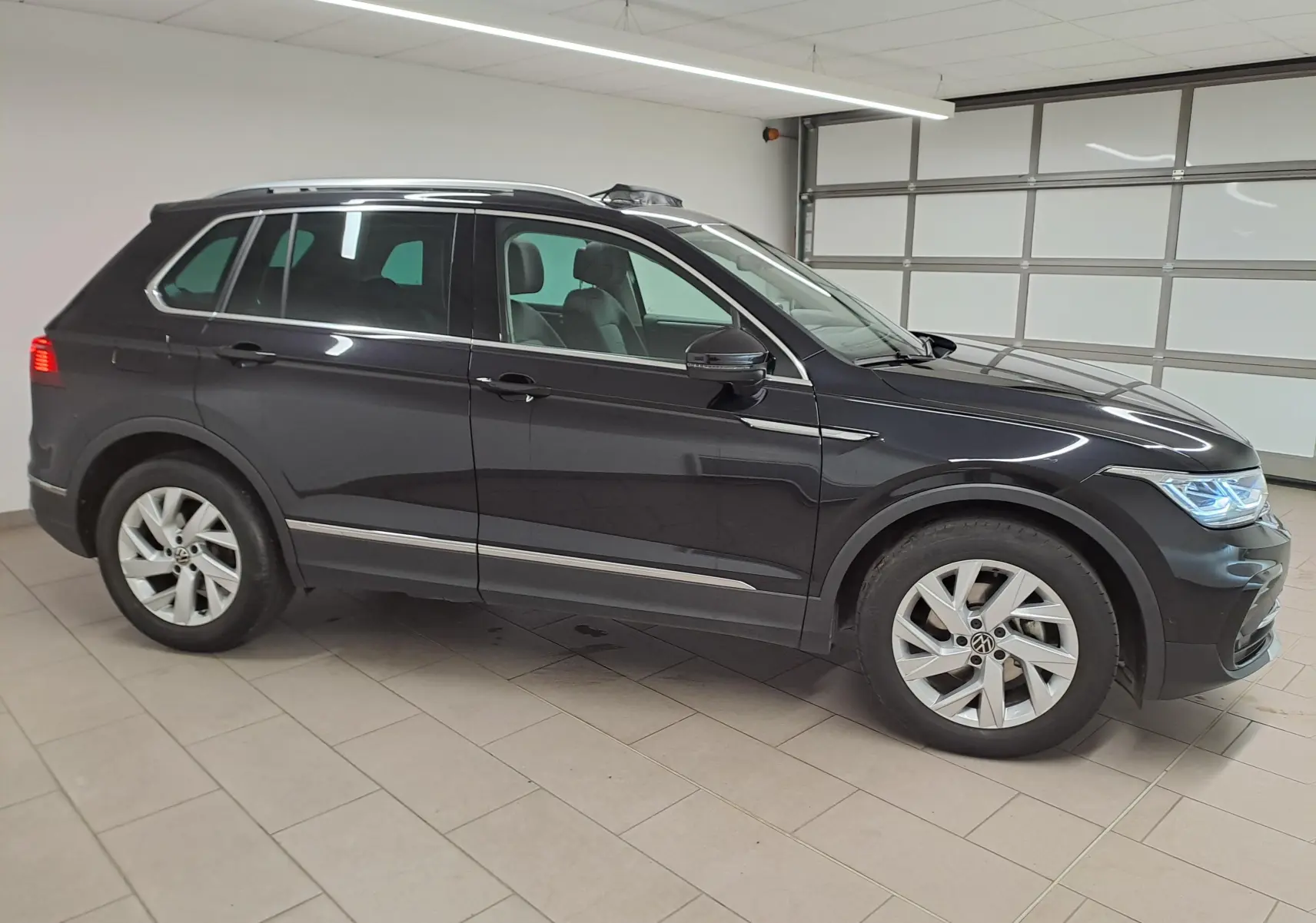 Vue de profil côté gauche du Volkswagen Tiguan 2022 noir intense avec attelage escamotable en garage intérieur.