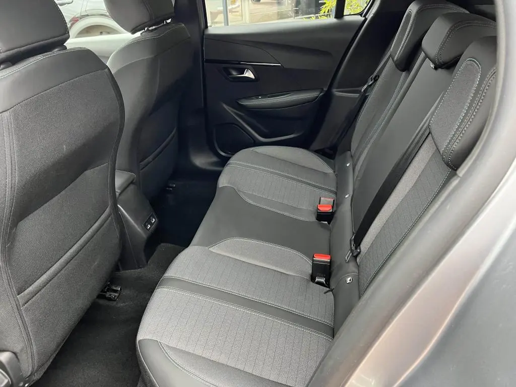 Vue intérieure arrière côté droit de la Peugeot 208 gris clair, sièges tissu noir avec surpiqûres grises et ceintures rouges.