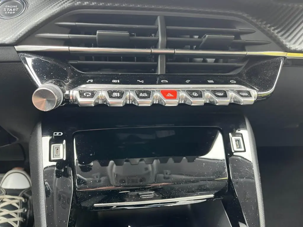 Vue rapprochée de la console centrale noire brillante de la Peugeot 208 2022 avec boutons métallisés et prise USB visible.