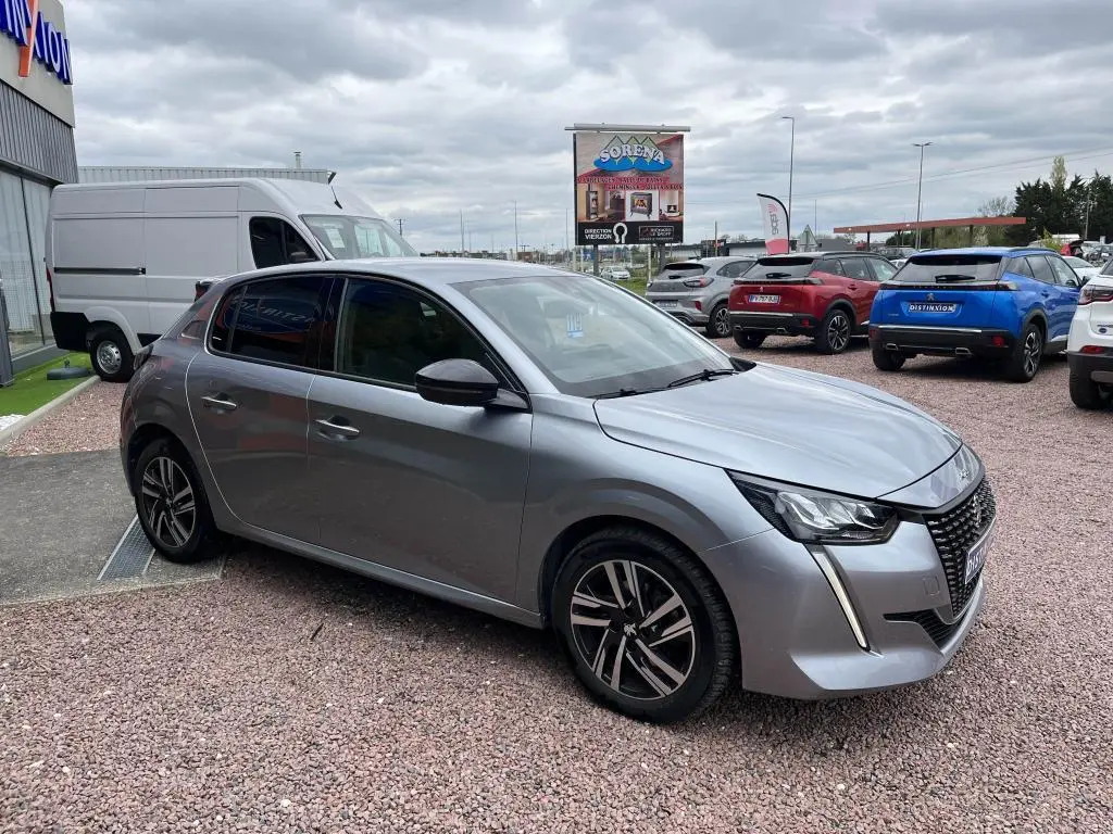 Peugeot 208 gris clair vue 3/4 avant droit, avec phares LED et jantes alliage distinctives.