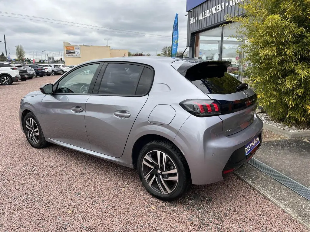 Peugeot 208 gris clair vue 3/4 arrière droit, avec vitres surteintées et jantes alliage distinctives.
