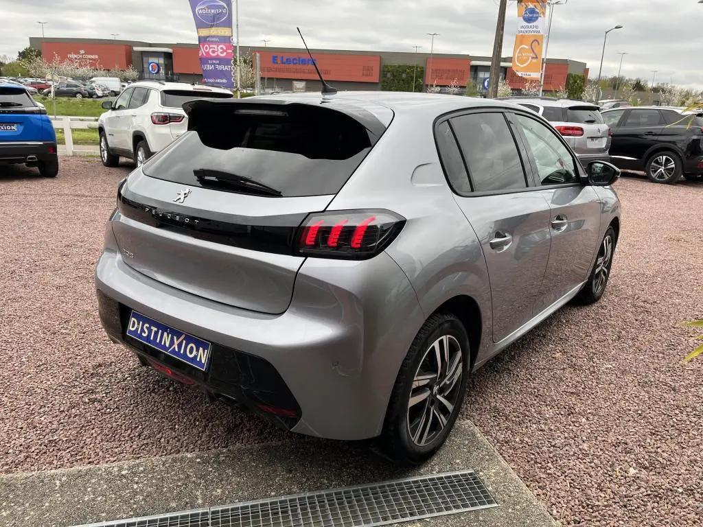 Peugeot 208 gris clair vue 3/4 arrière droit, avec feux arrière à griffes rouges et jantes alliage bicolores.