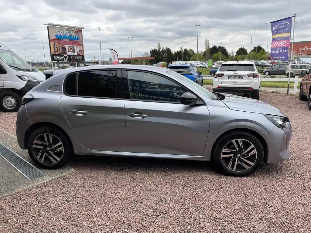 Peugeot 208 gris clair vue de profil côté gauche, avec vitres arrière surteintées et jantes alliage.