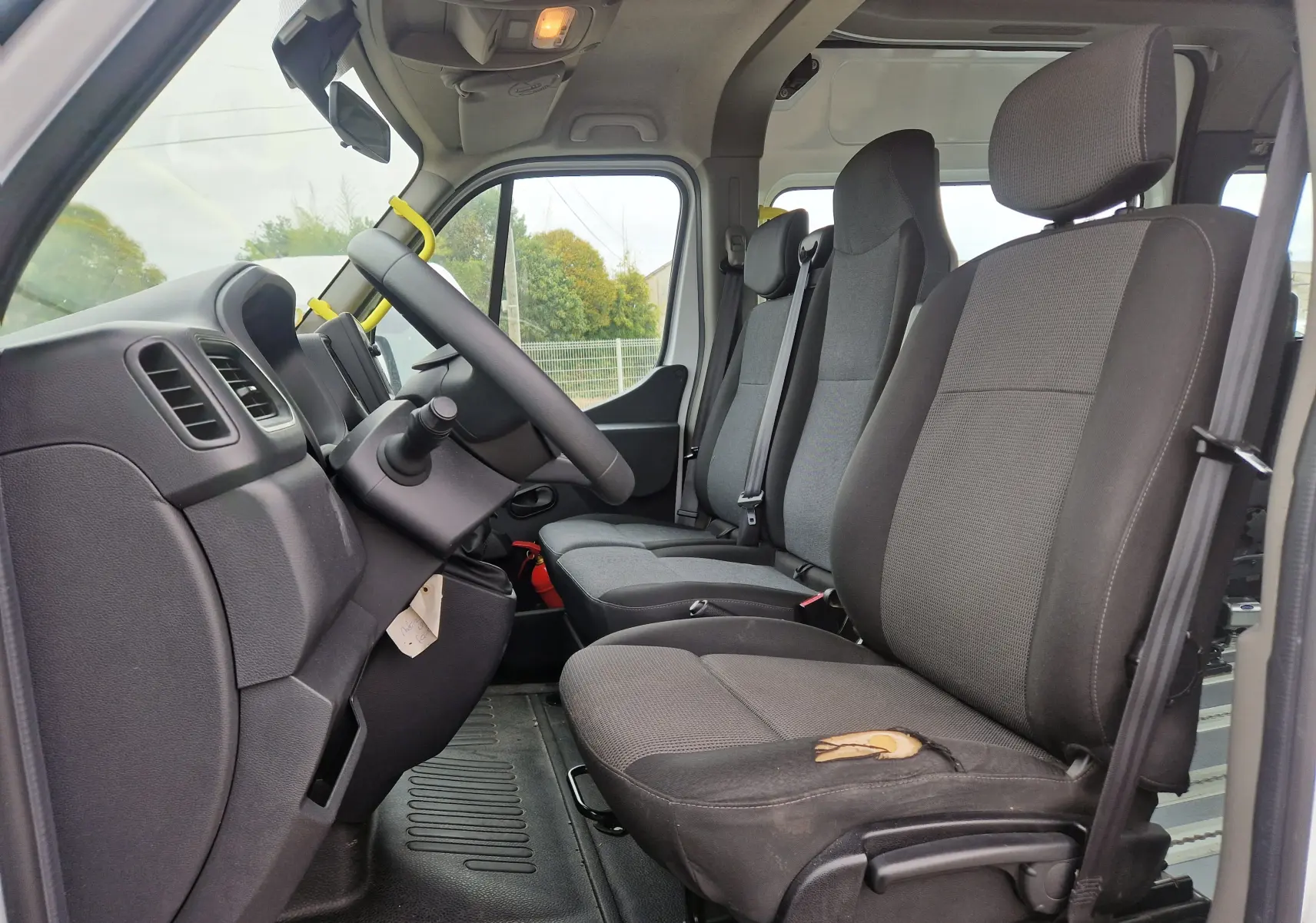Vue intérieure côté conducteur du Renault Master blanc 2020, montrant les sièges avant en tissu gris avec usure visible sur l'assise.