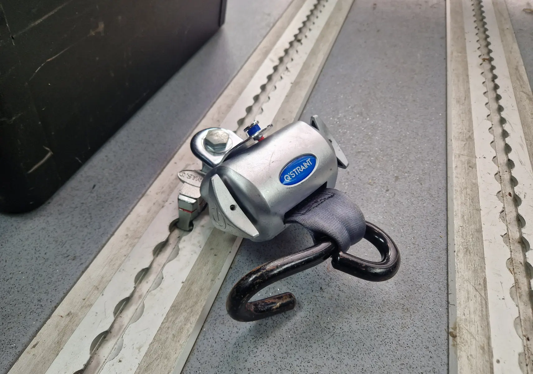 Gros plan sur un système d’arrimage Q'STRAINT fixé au sol gris à l’intérieur d’un Renault Master blanc TPMR.