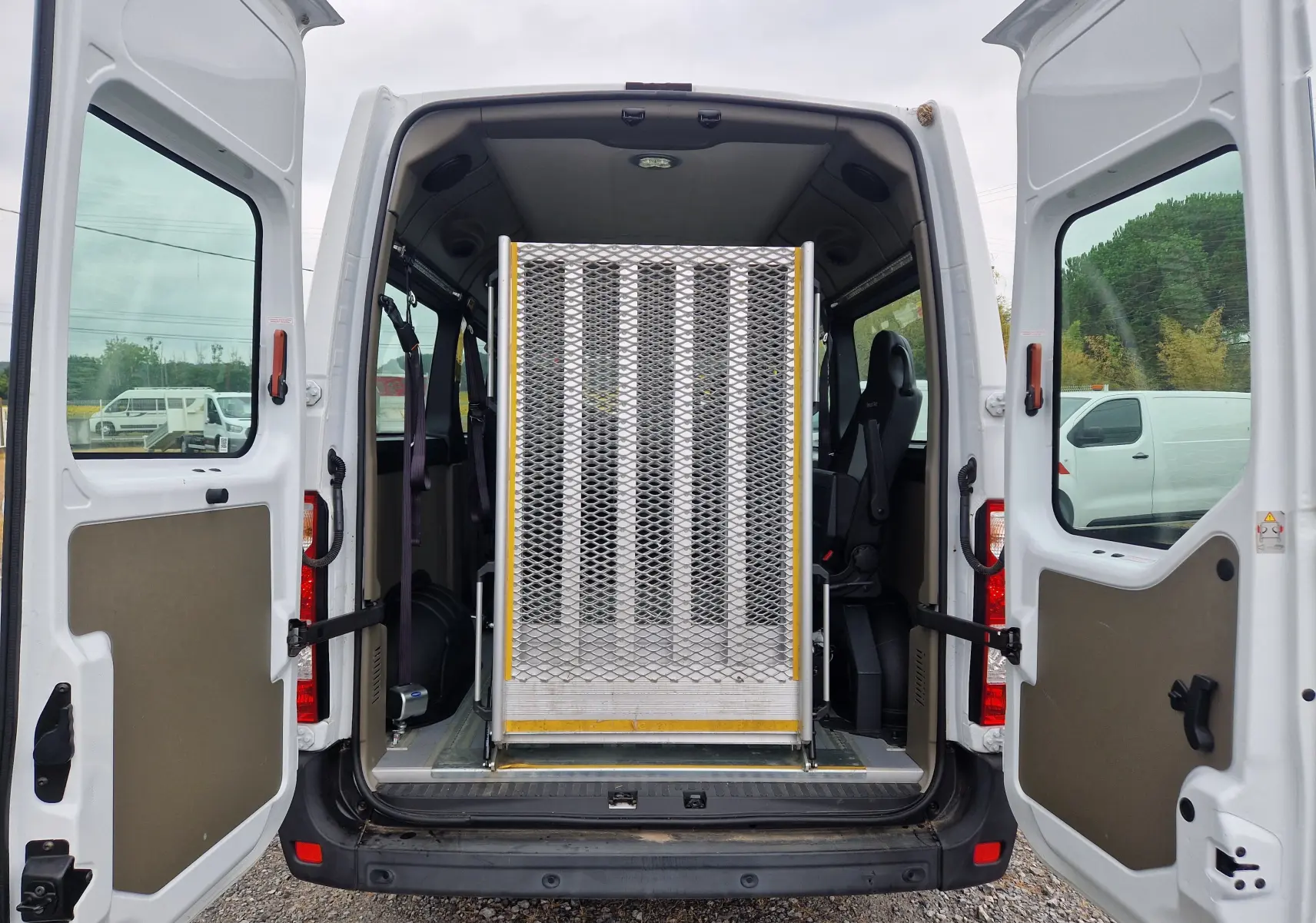 Vue arrière du Renault Master blanc 2020 avec portes ouvertes, montrant la rampe arrière métallique pour fauteuil roulant.