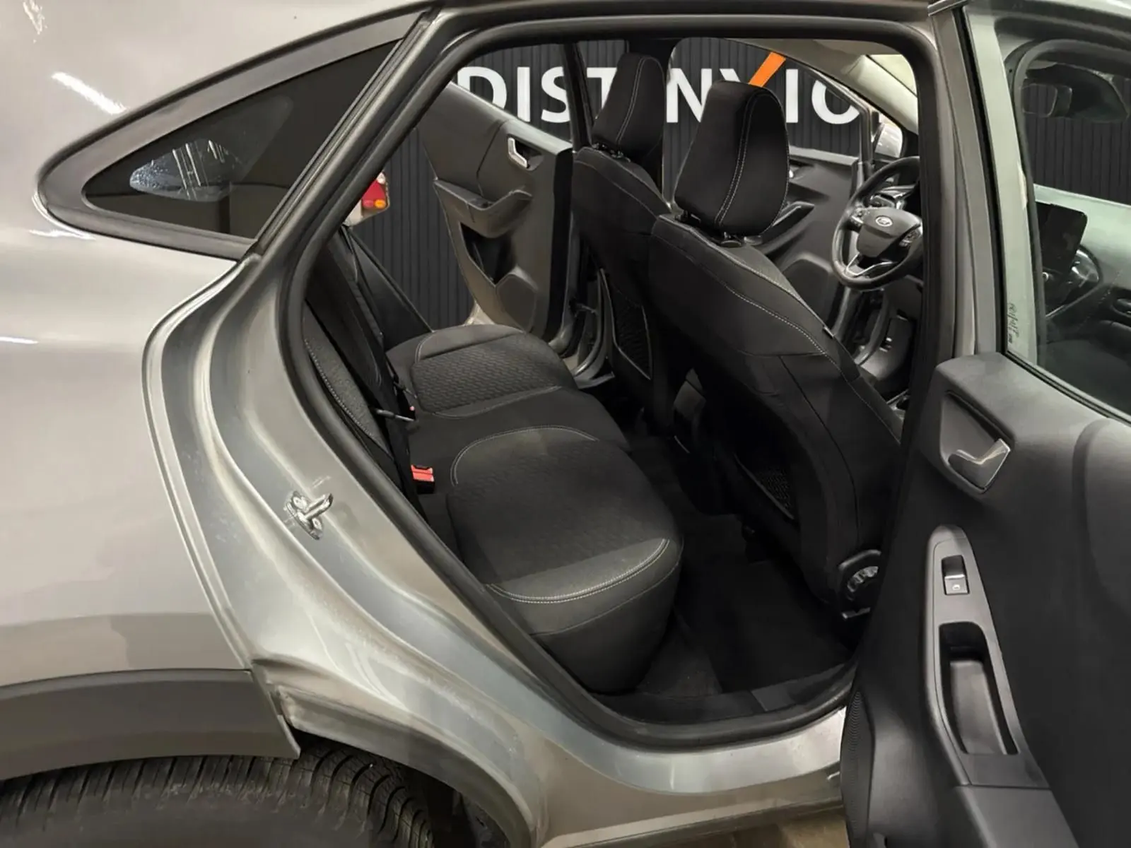 Vue intérieure côté gauche arrière du Ford Puma gris Solar 2023, montrant les sièges arrière et l'avant avec volant multifonction.
