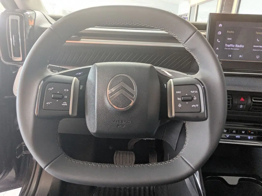Vue rapprochée du volant noir du Citroën E-C3 Aircross 2025 avec commandes intégrées et tableau de bord moderne.