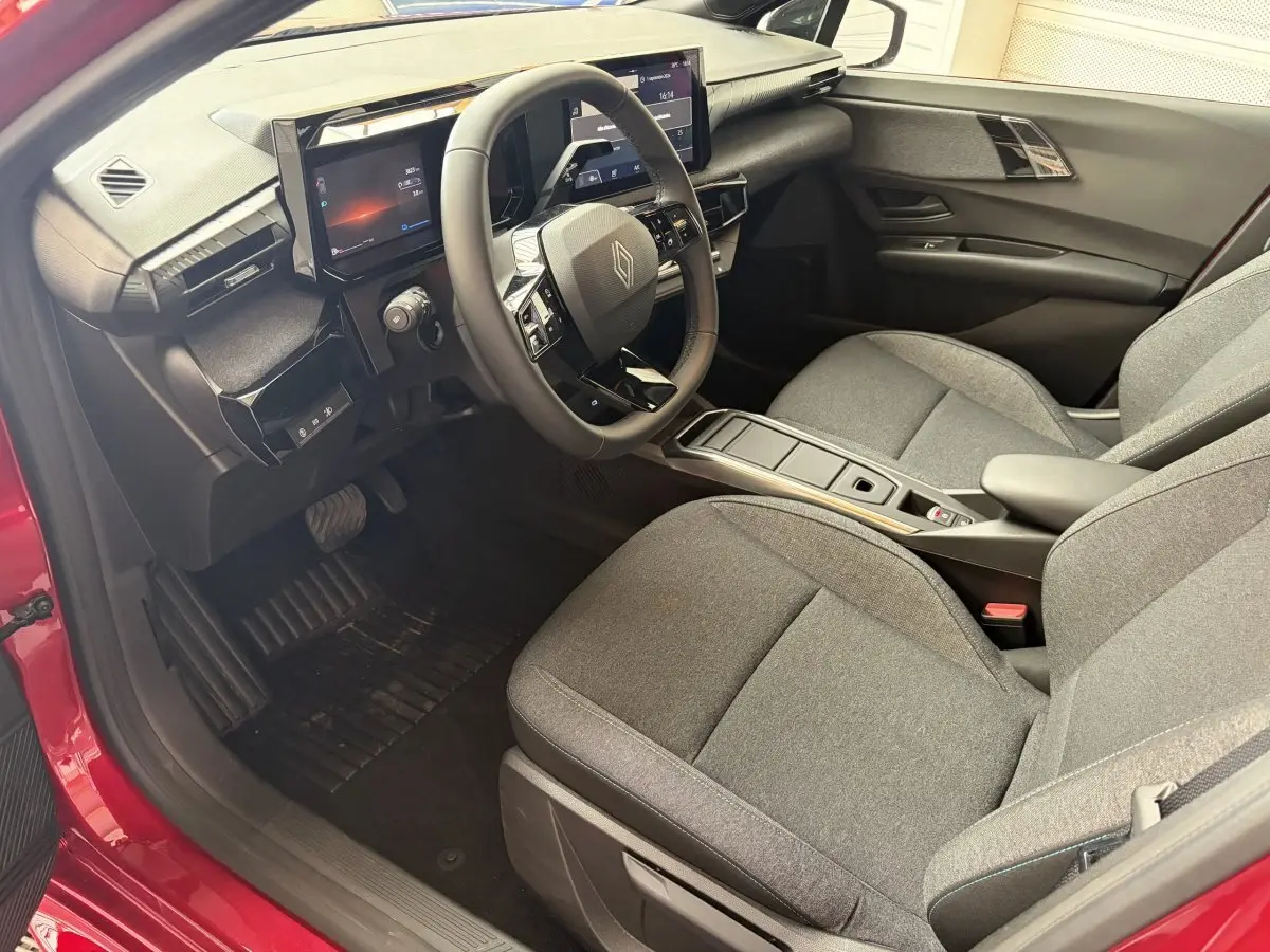 Intérieur avant droit de la Renault Clio Evolution rouge 2025, avec tableau de bord numérique et sièges tissu gris.
