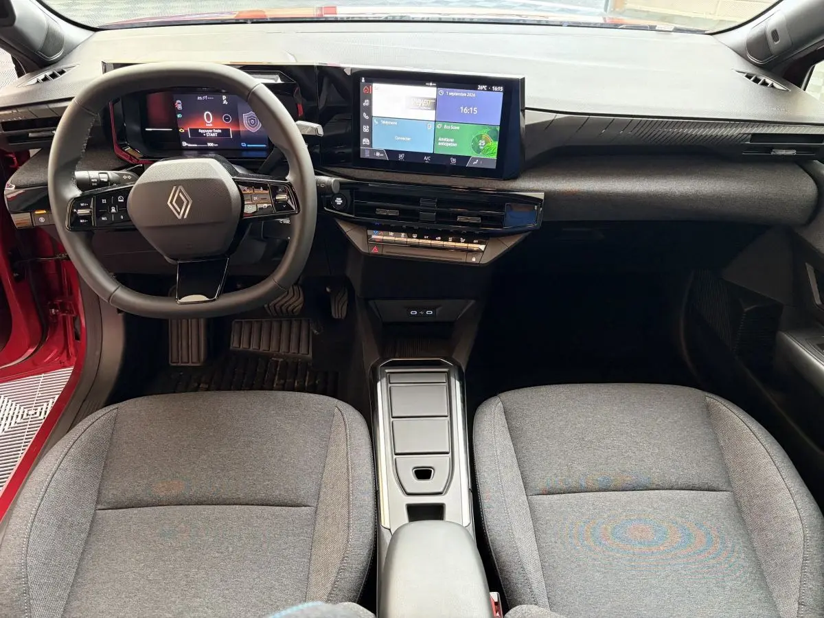 Vue intérieure avant de la Renault Clio 2025 rouge, avec tableau de bord numérique et écran tactile central.