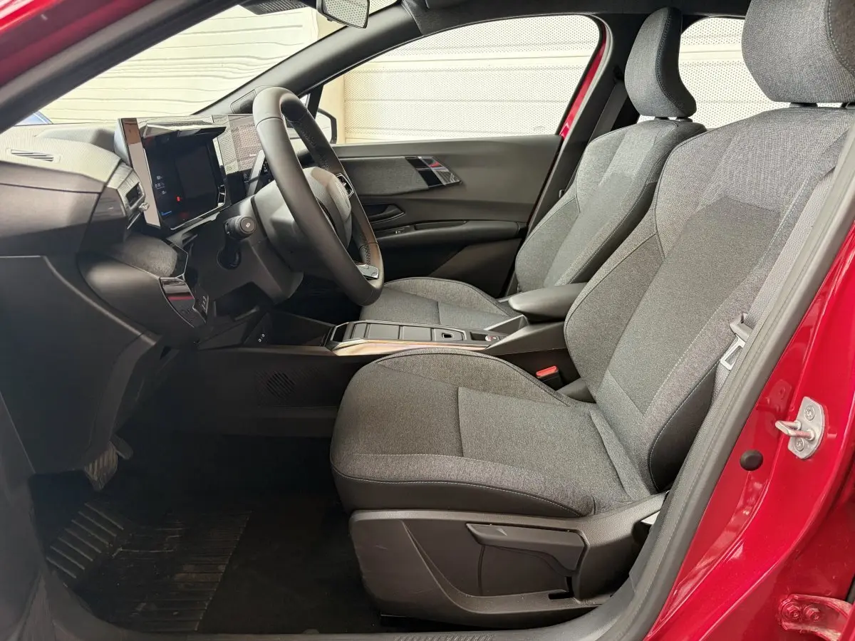 Intérieur côté conducteur de la Renault Clio rouge 2025, montrant sièges gris et tableau de bord moderne avec écran tactile.