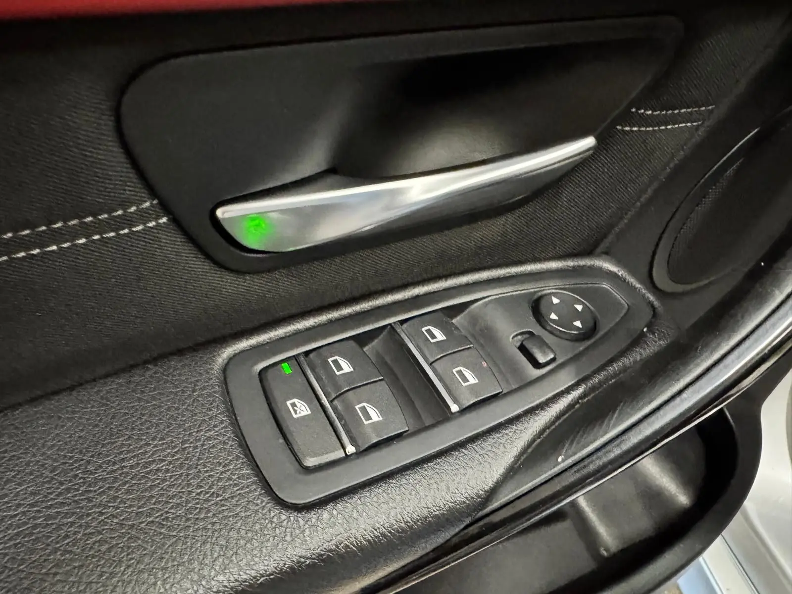 Détail de la commande des vitres électriques sur la portière noire côté conducteur d'une BMW Série 3 Touring gris aluminium.