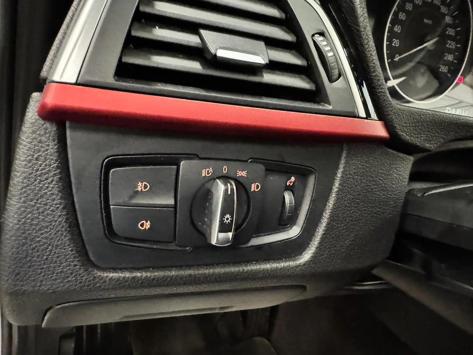 Gros plan sur le bouton de commande des phares avec bande décorative rouge dans l’habitacle noir d’une BMW Série 3 Touring F31.