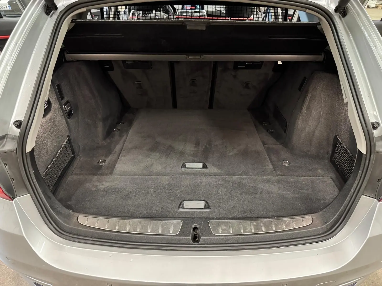 Vue arrière du coffre spacieux et vide d'une BMW Série 3 Touring F31 gris aluminium, avec tapis noir et filet latéral.