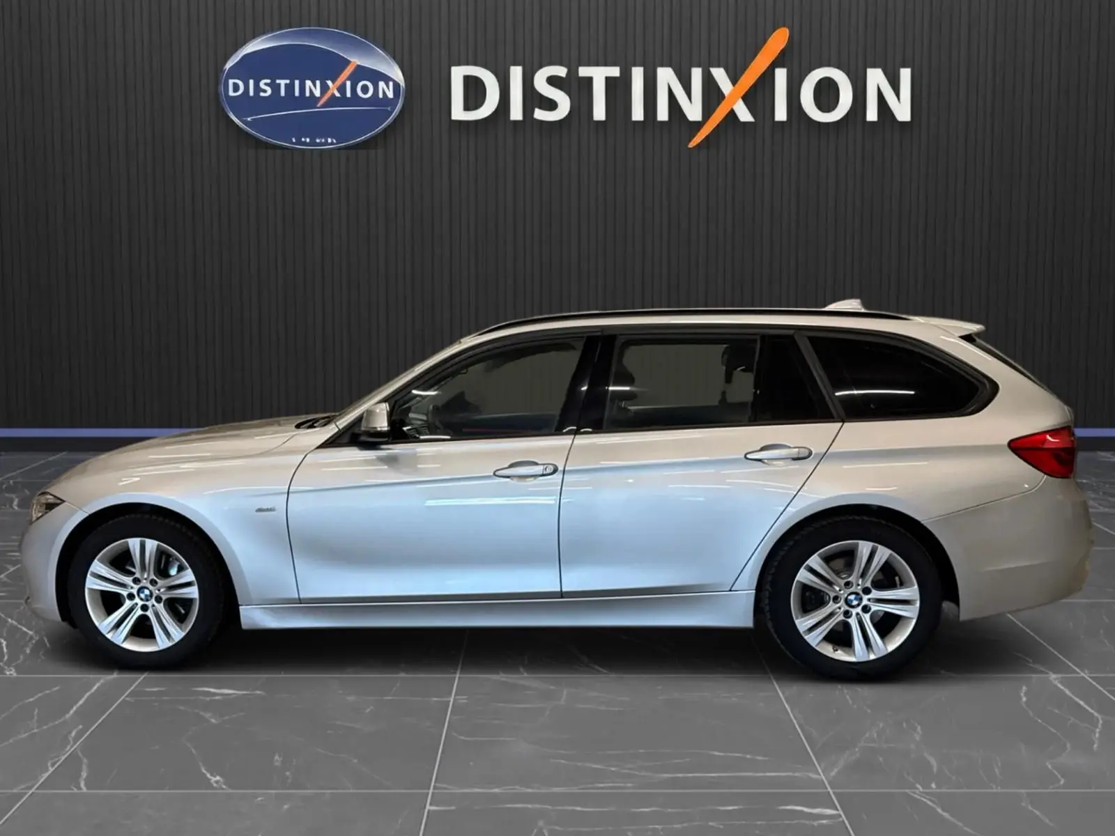 BMW Série 3 Touring F31 gris aluminium vue de profil côté gauche, avec jantes alliage et attelage électrique visible.