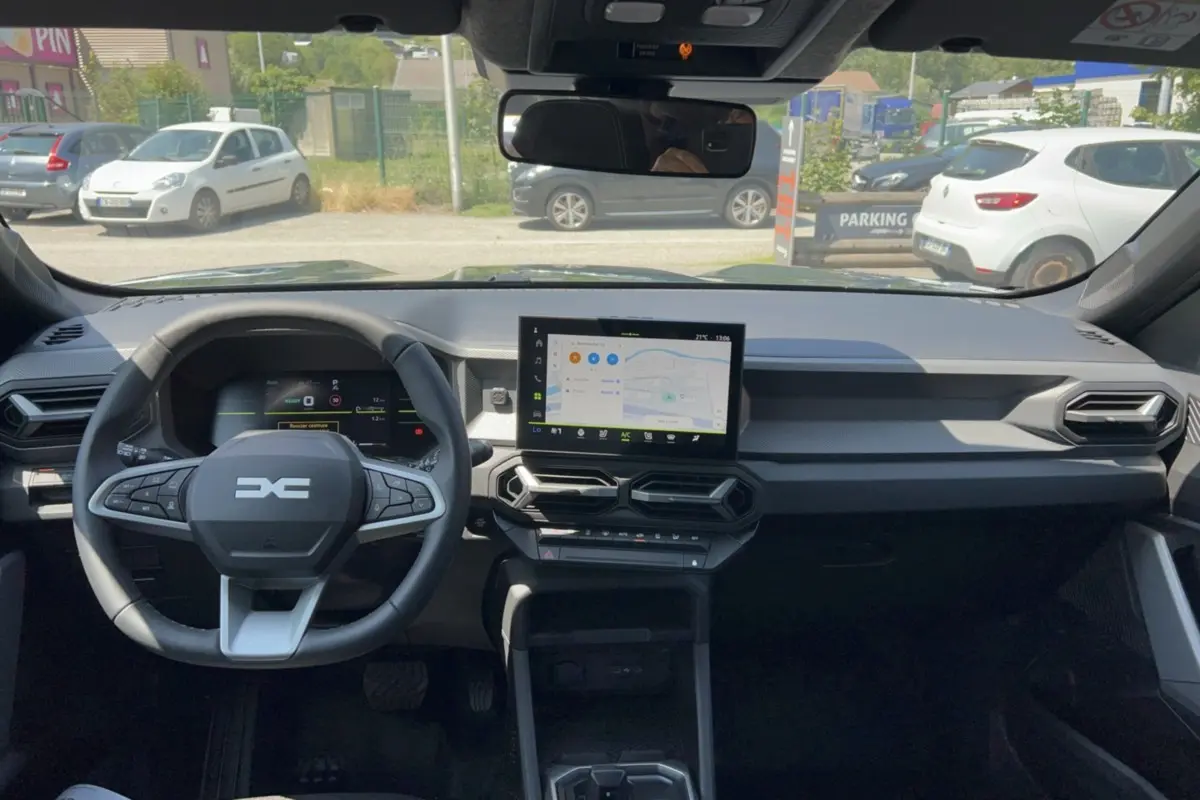 Vue intérieure frontale du tableau de bord du Dacia Duster Hybrid-G 150 avec écran central tactile et volant multifonction.