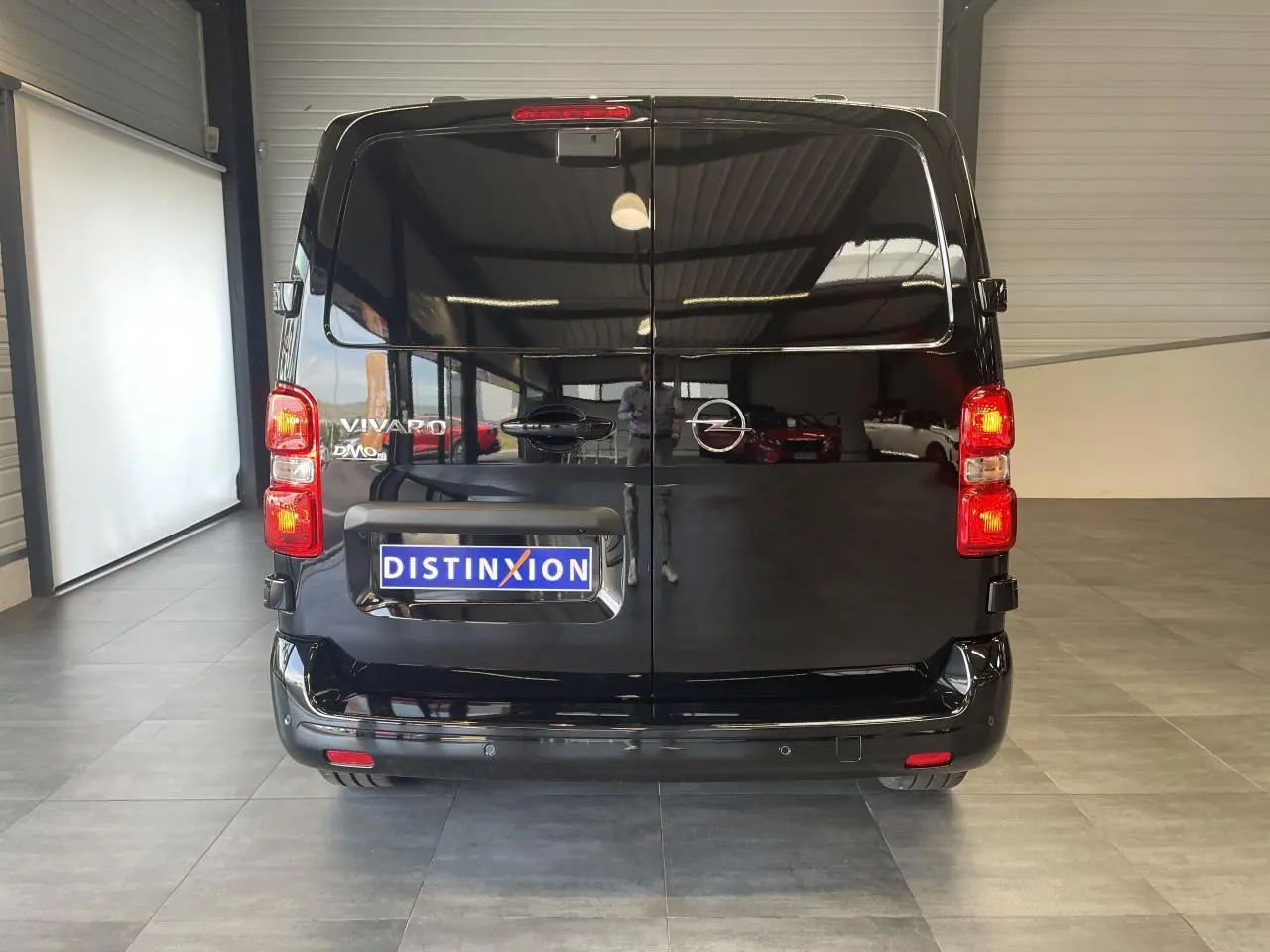Vue arrière d'un Opel Vivaro noir carbone avec feux arrière allumés et plaque Distinxion dans un showroom.