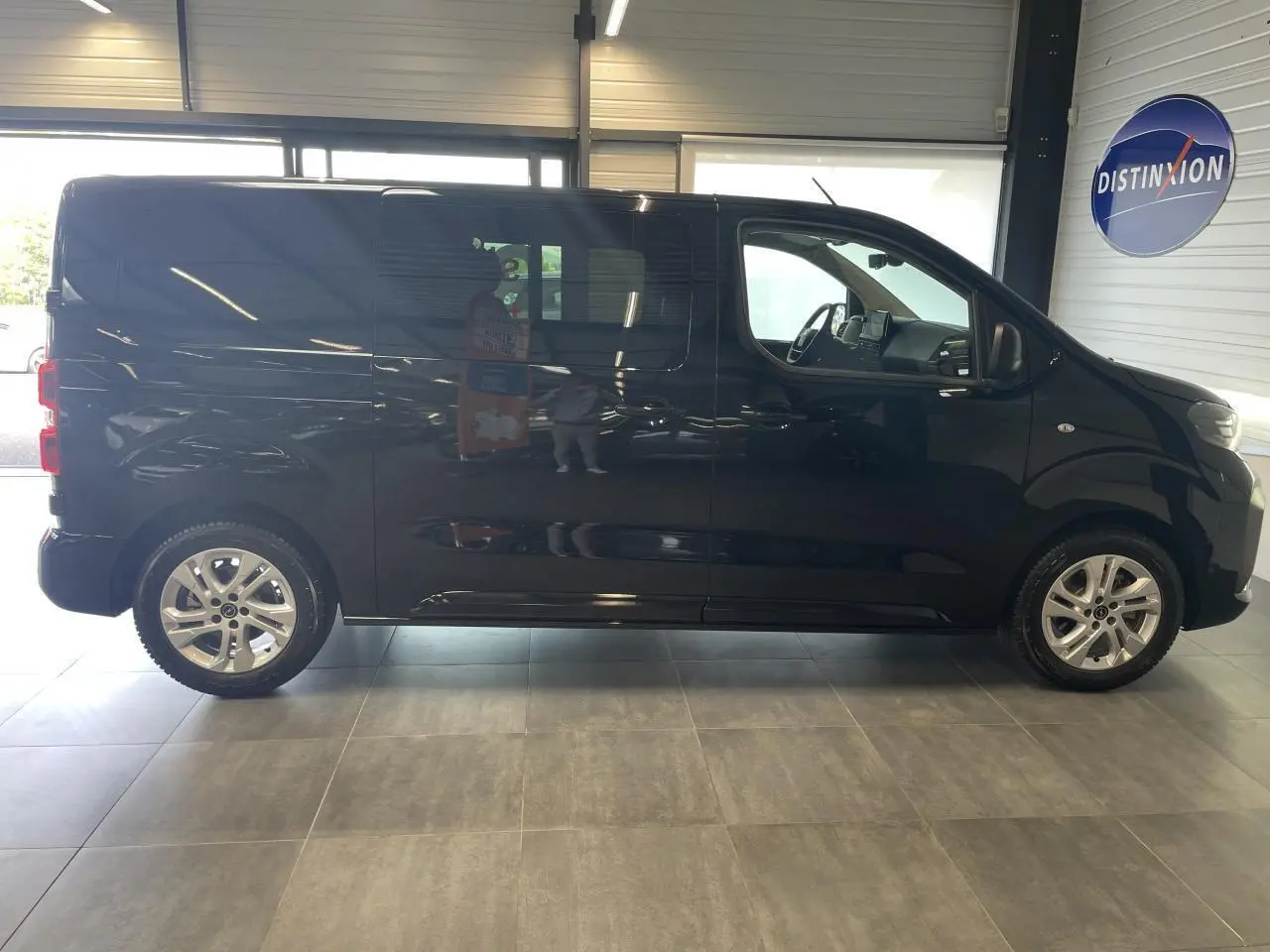 Profil droit d'un Opel Vivaro noir carbone double cabine 2025 avec jantes alliage et vitres surteintées en showroom.
