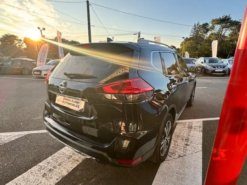 Vue 3/4 arrière droite d'un Nissan X-Trail noir intense 2018 avec barres de toit et feux arrière LED visibles.