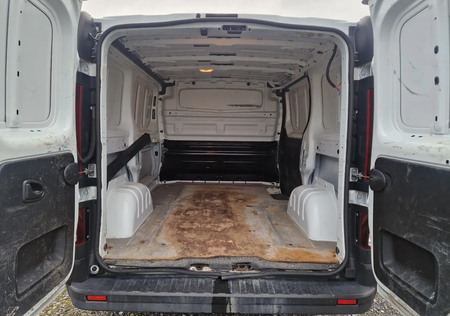 Vue arrière ouverte du Renault Trafic Fourgon blanc 2019, montrant l’espace de chargement vide avec plancher usé.