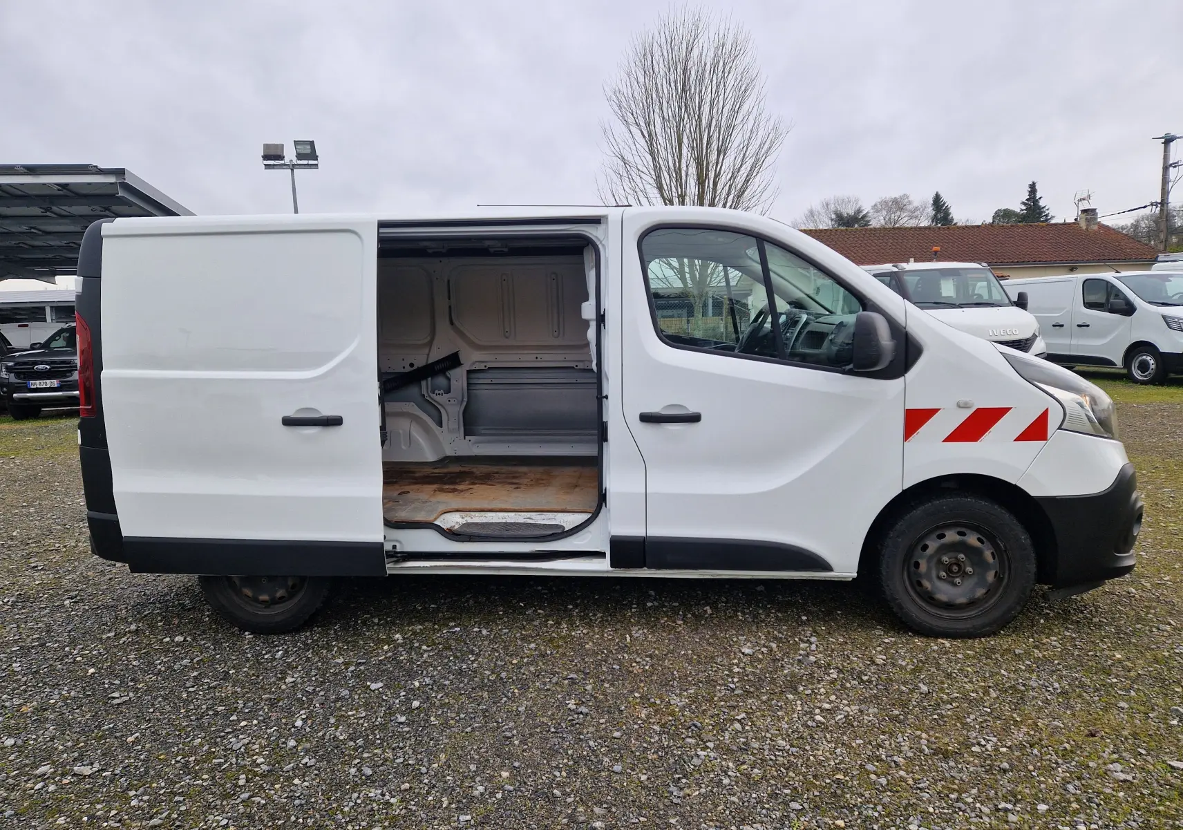 Vue de profil droit d’un Renault Trafic Fourgon blanc 2019 avec porte coulissante ouverte et bandes rouges diagonales sur l’aile avant.