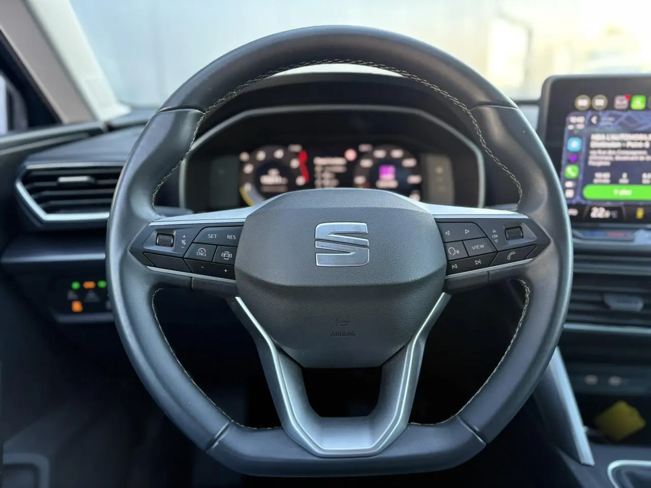 Volant cuir multifonction noir de la SEAT LEON ST 2.0 TDI 115 Style avec tableau de bord numérique en arrière-plan flou.