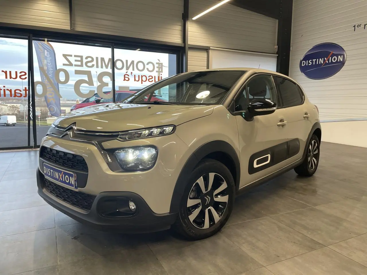 Citroën C3 beige clair vue 3/4 avant droit en intérieur, avec Airbump noir et jantes alliage bicolores.