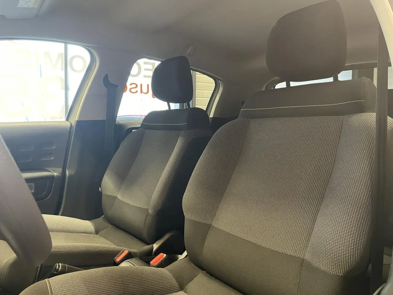 Vue intérieure des sièges avant en tissu gris avec surpiqûres jaunes de la Citroën C3 2024 beige clair.