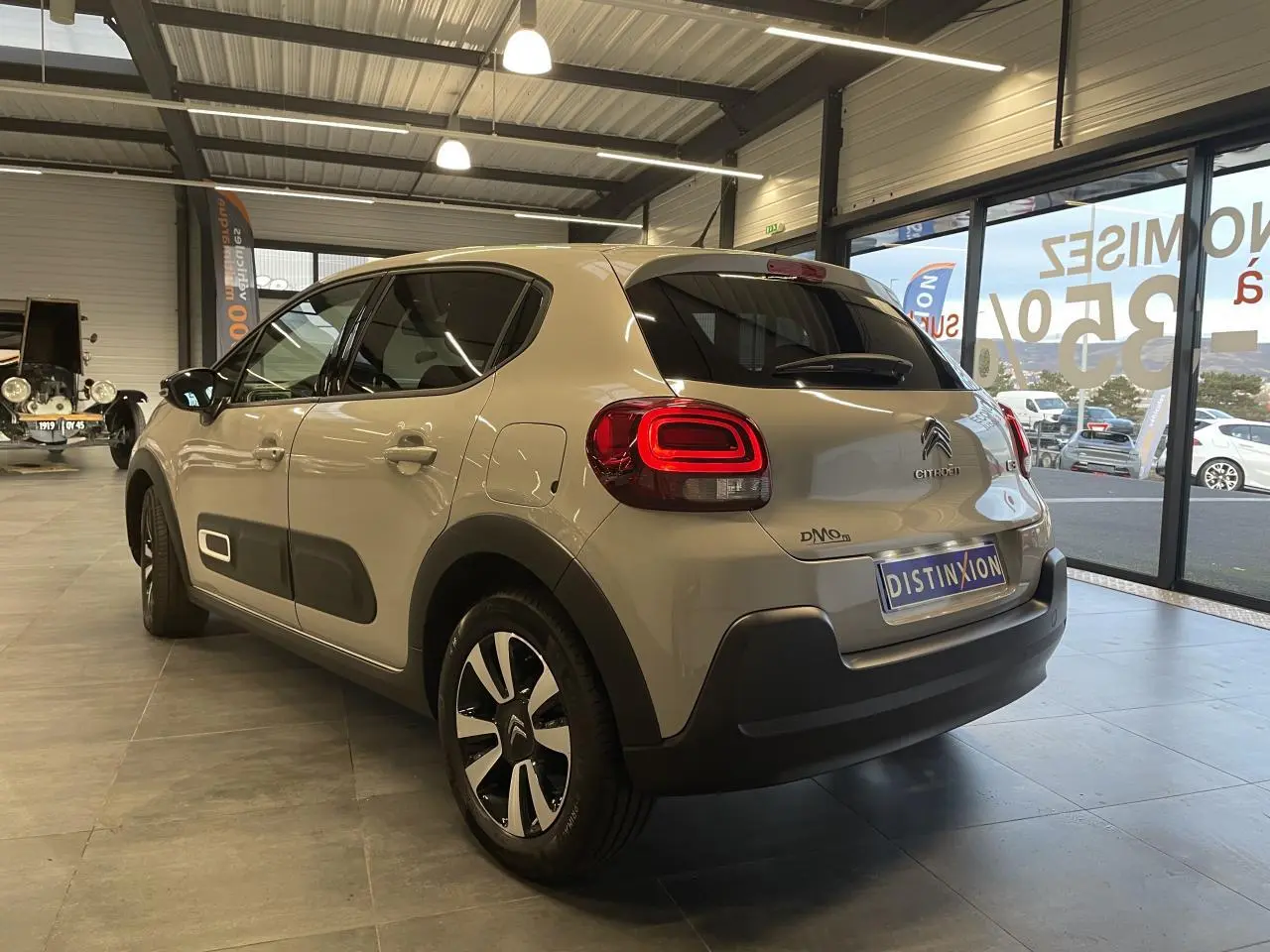 Vue 3/4 arrière droite d'une Citroën C3 beige clair avec feux arrière LED et protections latérales noires en showroom.
