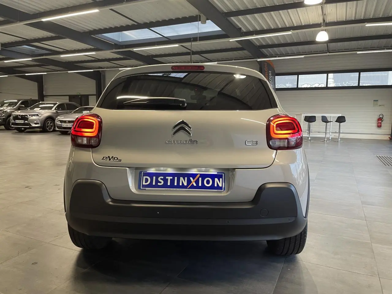 Vue arrière d'une Citroën C3 beige clair 2024 avec feux arrière LED et pare-chocs noir mat en intérieur showroom.