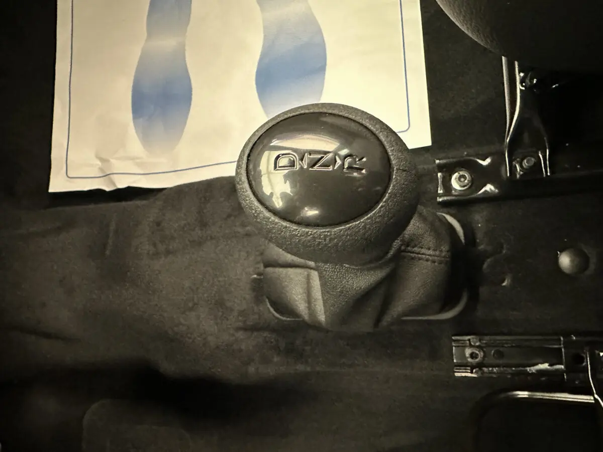 Gros plan sur le levier de vitesses noir de l'AIXAM AMBITION 0.5 CITY PACK 2026, intérieur sombre sans couleur visible.