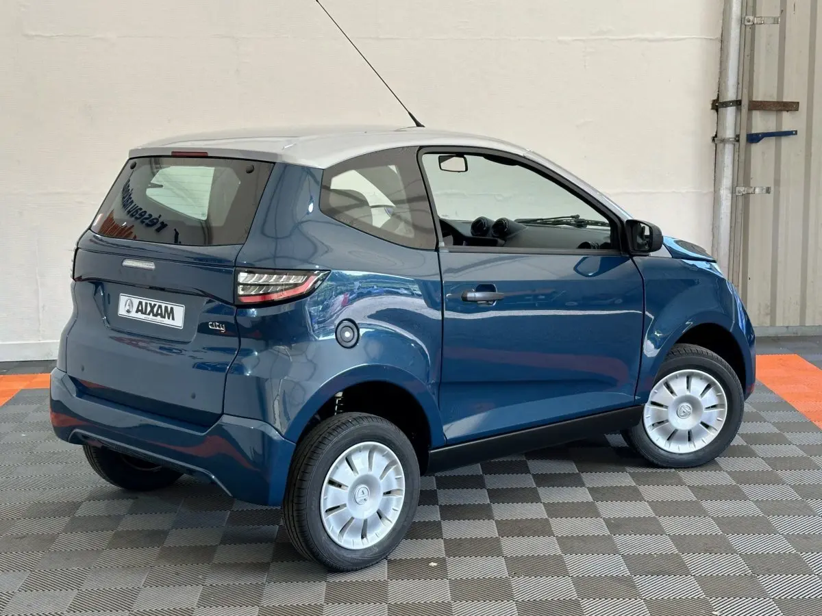 Vue 3/4 arrière droite de l'AIXAM Ambition 0.5 City Pack bleu avec toit blanc et caméra sur rétroviseur côté gauche.