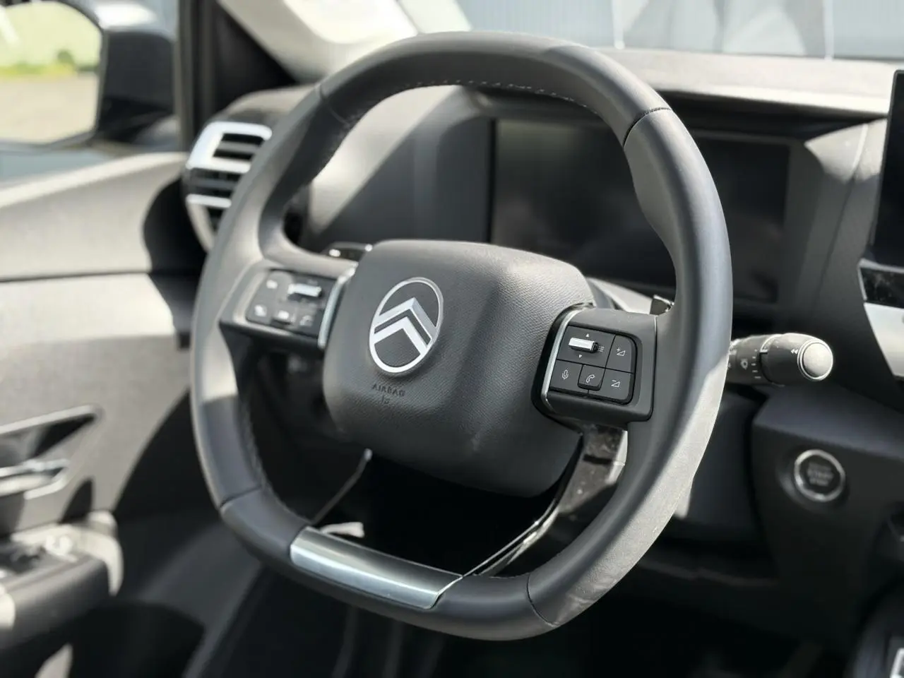 Vue rapprochée du volant cuir noir de la Citroën C4 Hybrid 2025 avec commandes intégrées et bouton de démarrage.