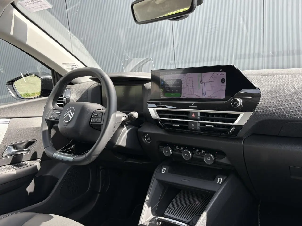 Vue intérieure côté conducteur du tableau de bord noir de la Citroën C4 Hybrid 2025 avec écran GPS tactile et volant multifonction.