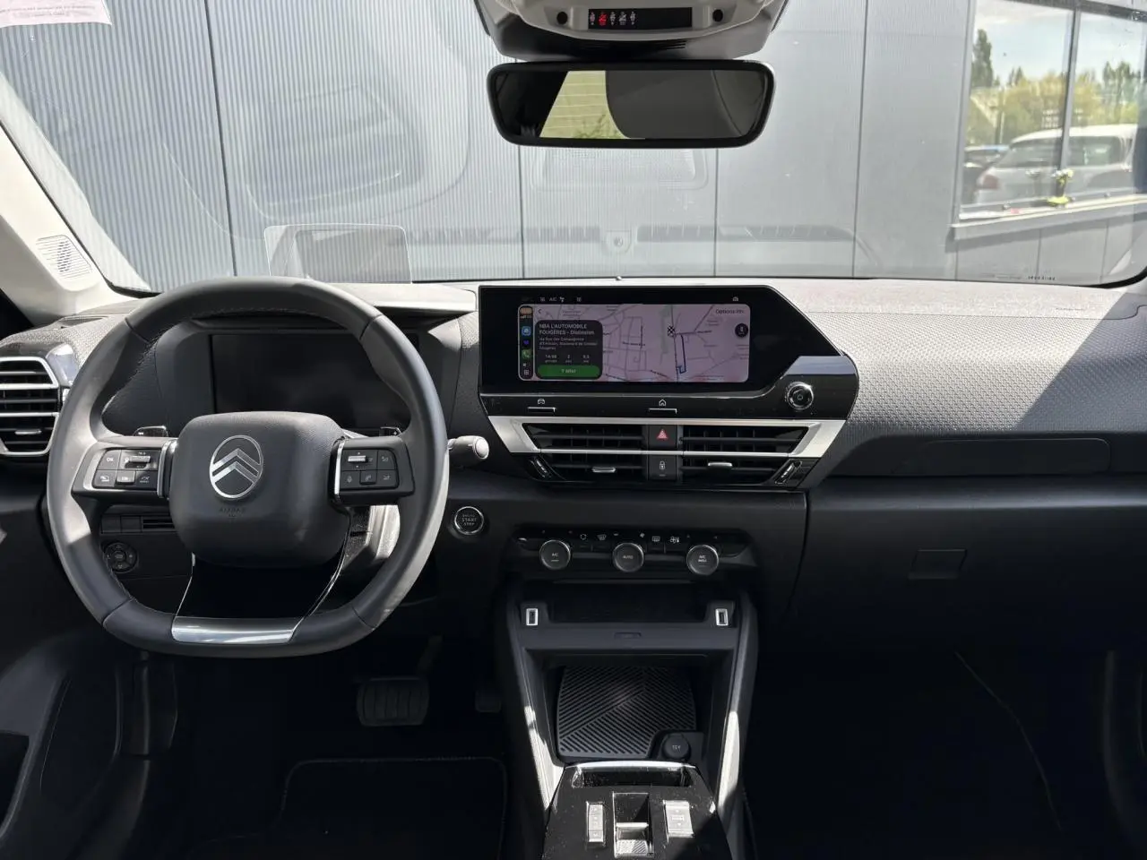 Vue intérieure avant du tableau de bord et volant noir de la Citroën C4 Hybrid 145 e-DSC6 Max avec écran tactile GPS allumé.