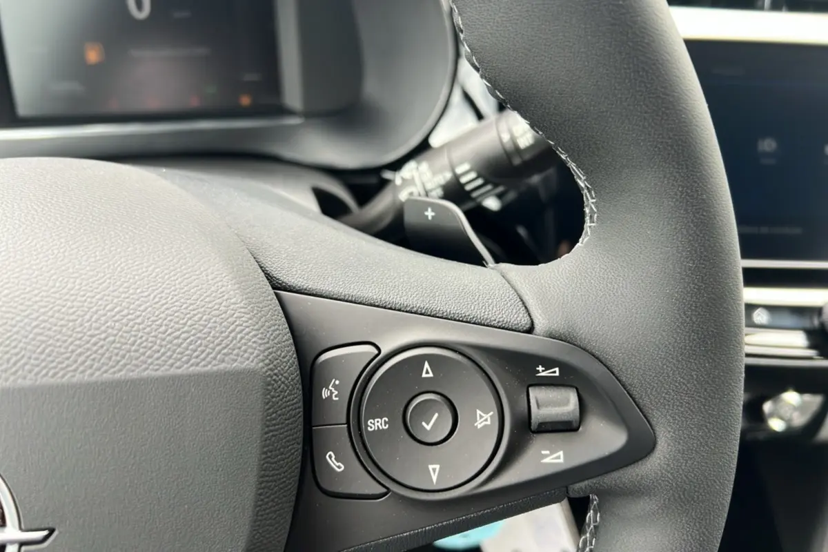 Gros plan sur les commandes multifonctions noires du volant cuir de l’Opel Corsa Hybrid blanc Kontur.
