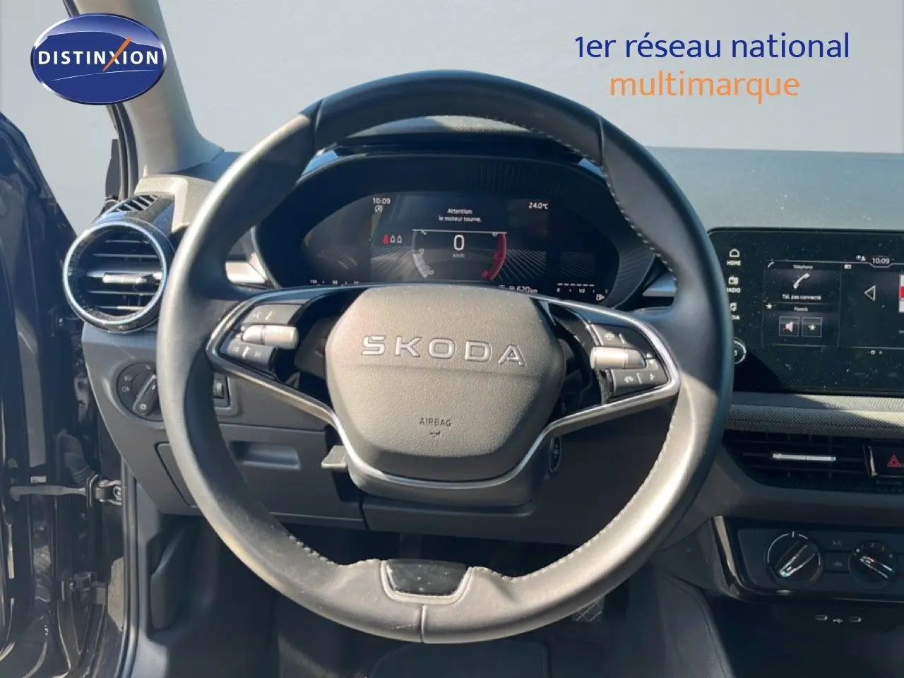 Vue intérieure centrée sur le volant SKODA d'une Fabia noire, avec tableau de bord numérique et écran tactile visible.