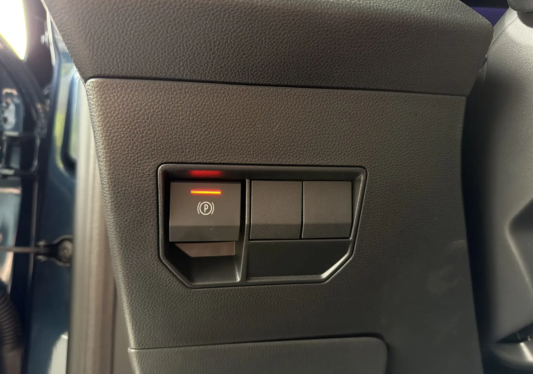 Gros plan sur le bouton de frein à main électrique allumé, côté gauche intérieur d'un Dacia Bigster Bleu Indigo 2026.
