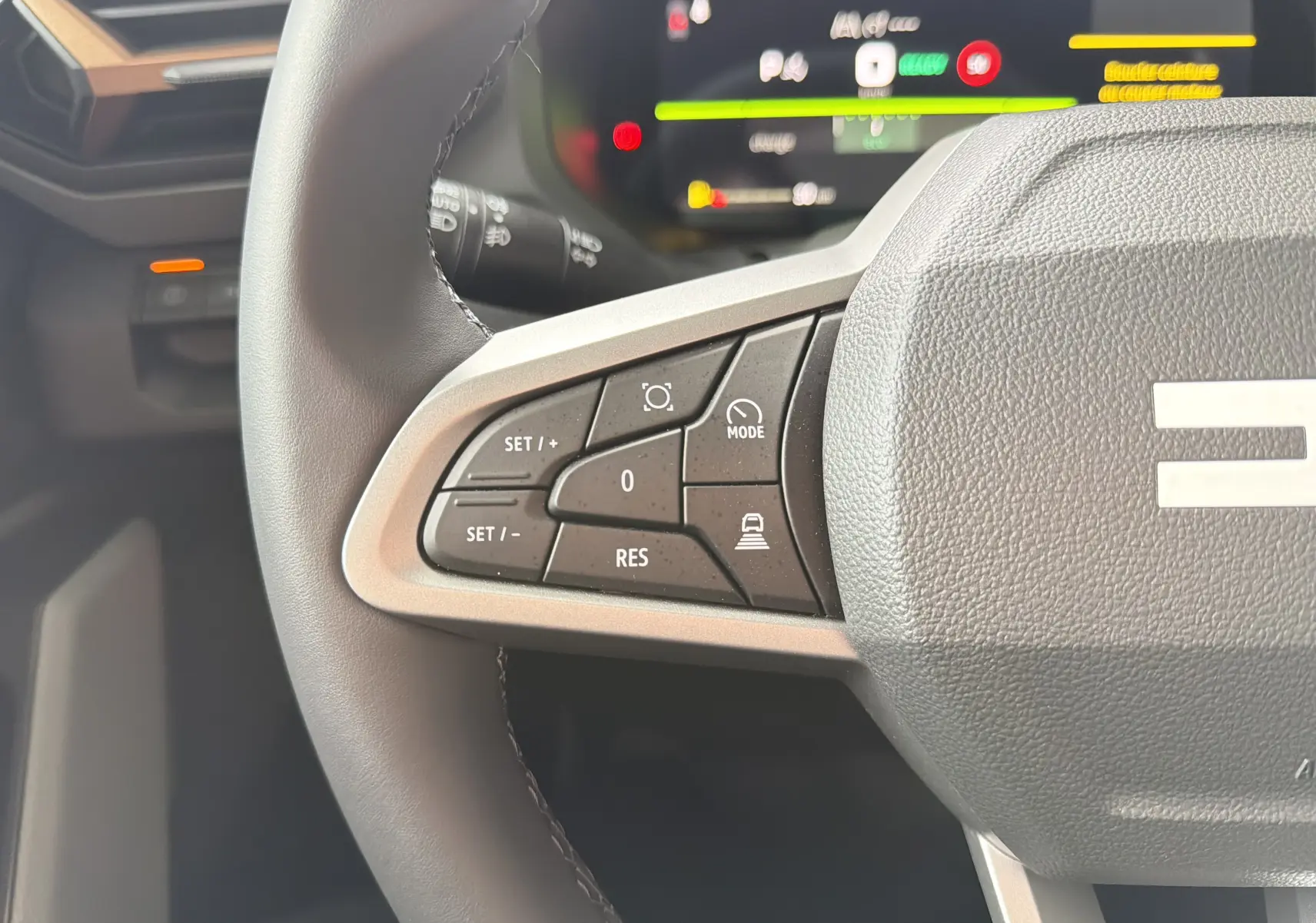 Gros plan sur les commandes à gauche du volant du Dacia Bigster Hybrid 155, intérieur noir avec affichage numérique flou.
